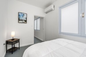 Une chambre d’hôtel avec un lit, une table de chevet avec une lampe, un tableau encadré au mur et un appareil de climatisation.