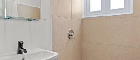 A bathroom with a white sink, a mirror, a shower, and a window.