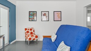 A modern living room with a blue sofa, a red and white patterned armchair, and three framed artworks on the wall.