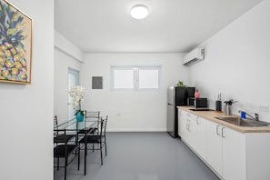 Ett modernt kök med vita skåp, en diskho i rostfritt stål och en mikrovågsugn. Det finns en matplats med ett glasbord och stolar, samt en vas med vita blommor.