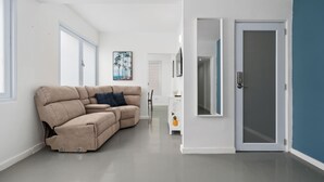 A modern living room with a beige sofa, a small white side table, and a door with a glass panel. - Otium Rentals Best Condado Location Near Beach (San Juan)