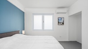A bedroom with a bed, a window, and an air conditioning unit. - Otium Rentals Best Condado Location Near Beach (San Juan)