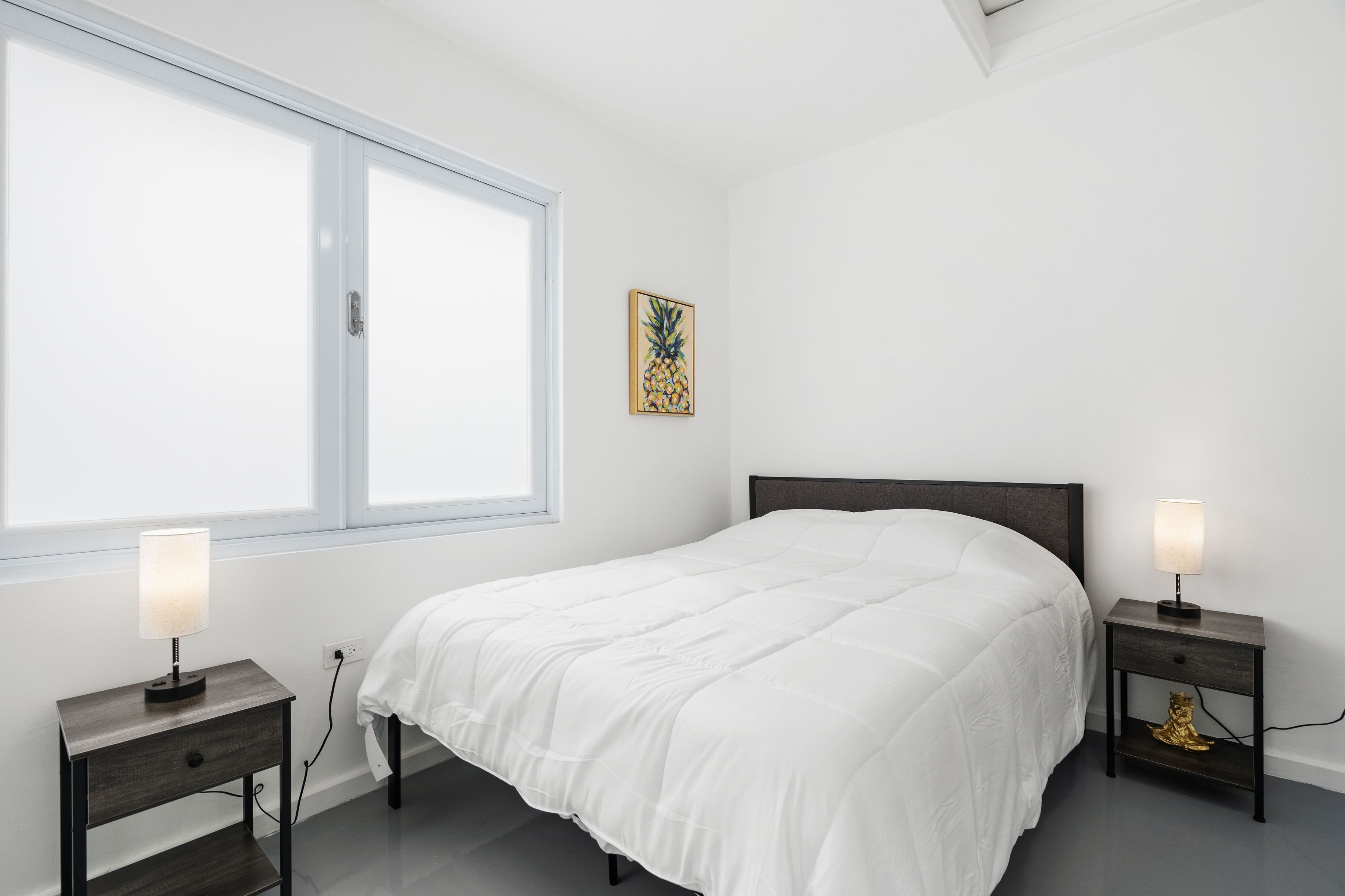 Een slaapkamer met een groot bed, twee nachtkastjes met lampen, een raam en een kunstwerk aan de muur.