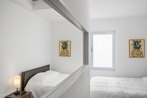 A bedroom with two beds, a nightstand with a lamp, and two abstract paintings on the walls.
