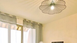 A living room with a sofa, a TV on a wooden cabinet, a ceiling fan, and a balcony with chairs. - Sea View Apartment in Saint-Clair, 400 m from the beach! (Le Lavandou)