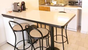 A modern kitchen with a central island, black chairs, and a white countertop. - Sea View Apartment in Saint-Clair, 400 m from the beach! (Le Lavandou)