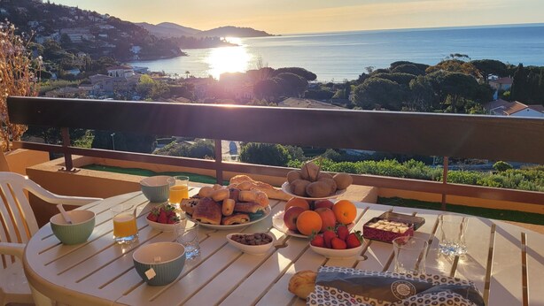 A balcony table with breakfast items, a chair, and a scenic view of the sea and hills. - Sea View Apartment in Saint-Clair, 400 m from the beach! (Le Lavandou)