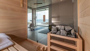 A sauna room with wooden walls, a glass door leading to an outdoor area with exercise equipment, and a wooden bench with stones.