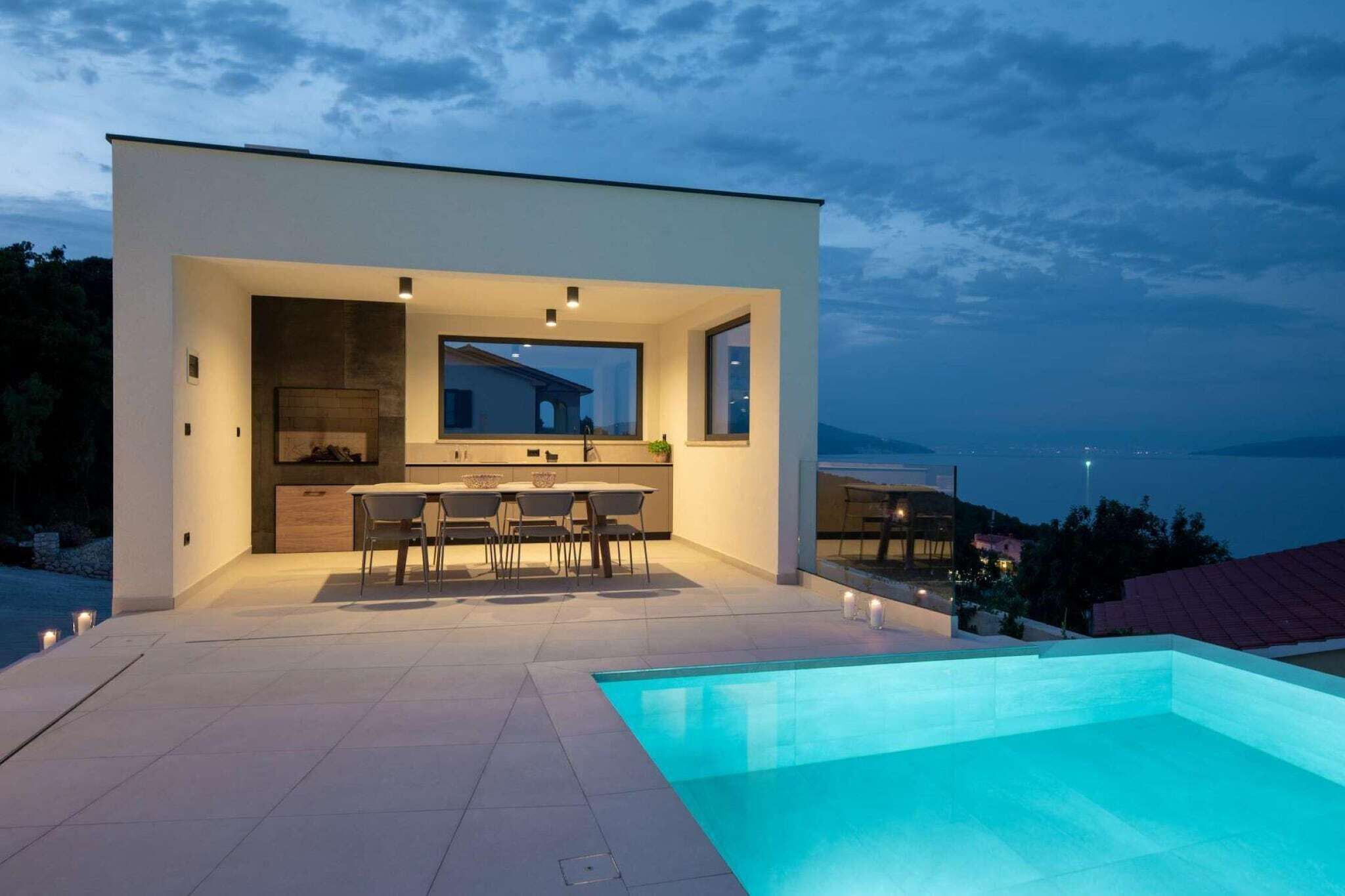 A modern house with an outdoor pool, a dining area, and a view of the sea.