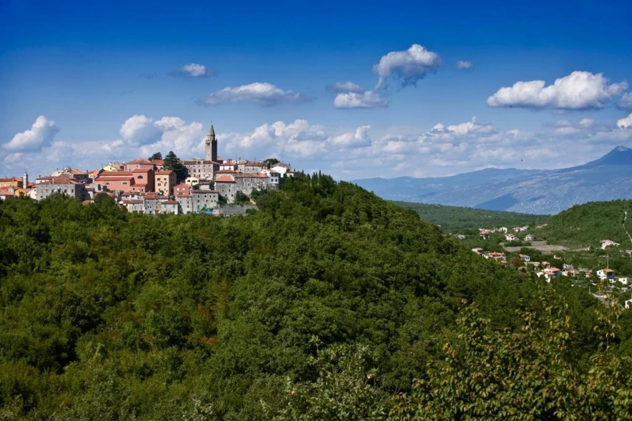 A historic town with a prominent church on a hill, surrounded by lush greenery and a clear sky.