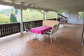 Een overdekt terras met een tafel en stoelen, en uitzicht op de omgeving, met een geplaveid terras.
