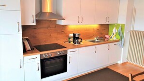 Una cocina compacta con armarios blancos, una campana extractora de acero inoxidable, horno empotrado y encimera de madera.