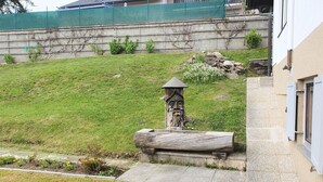 Un jardín con una escultura de madera, un banco de piedra y una casa al fondo.