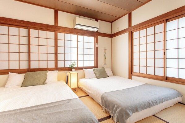A traditional Japanese-style room with tatami flooring, two beds with tatami mats, a shoji screen door, and a ceiling-mounted air conditioning unit.