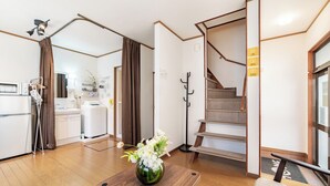 Ein modernes Hotelzimmer mit Holzboden, einem Holztisch mit Blumenvase, einer Treppe und einer Küchenzeile im Hintergrund.