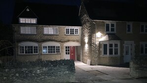 A two-story stone building with a red door, multiple windows, and a paved driveway.