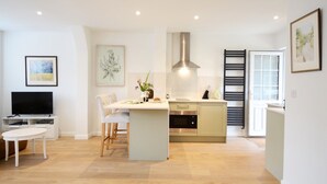 A modern kitchen with a central island, a dining area with a white table and chairs, and a TV on a white stand.