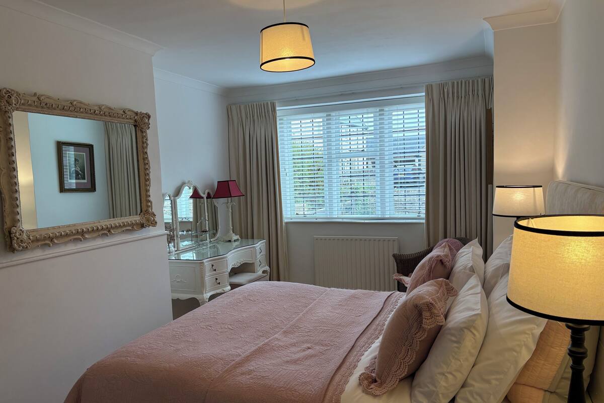 A bedroom with a bed, a dresser, a mirror, a window with curtains, and a lamp.