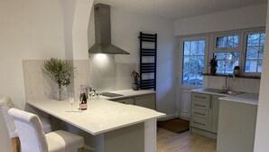 A modern kitchen with a central island, bar stools, a built-in stove hood, and a window overlooking a snowy landscape.