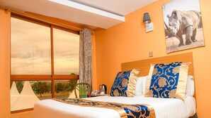 A hotel room with a large bed, a view of the sky through the window, a mounted picture of a rhinoceros, and a lamp on the wall. - Eaglesvale Resort Naivasha (Naivasha)