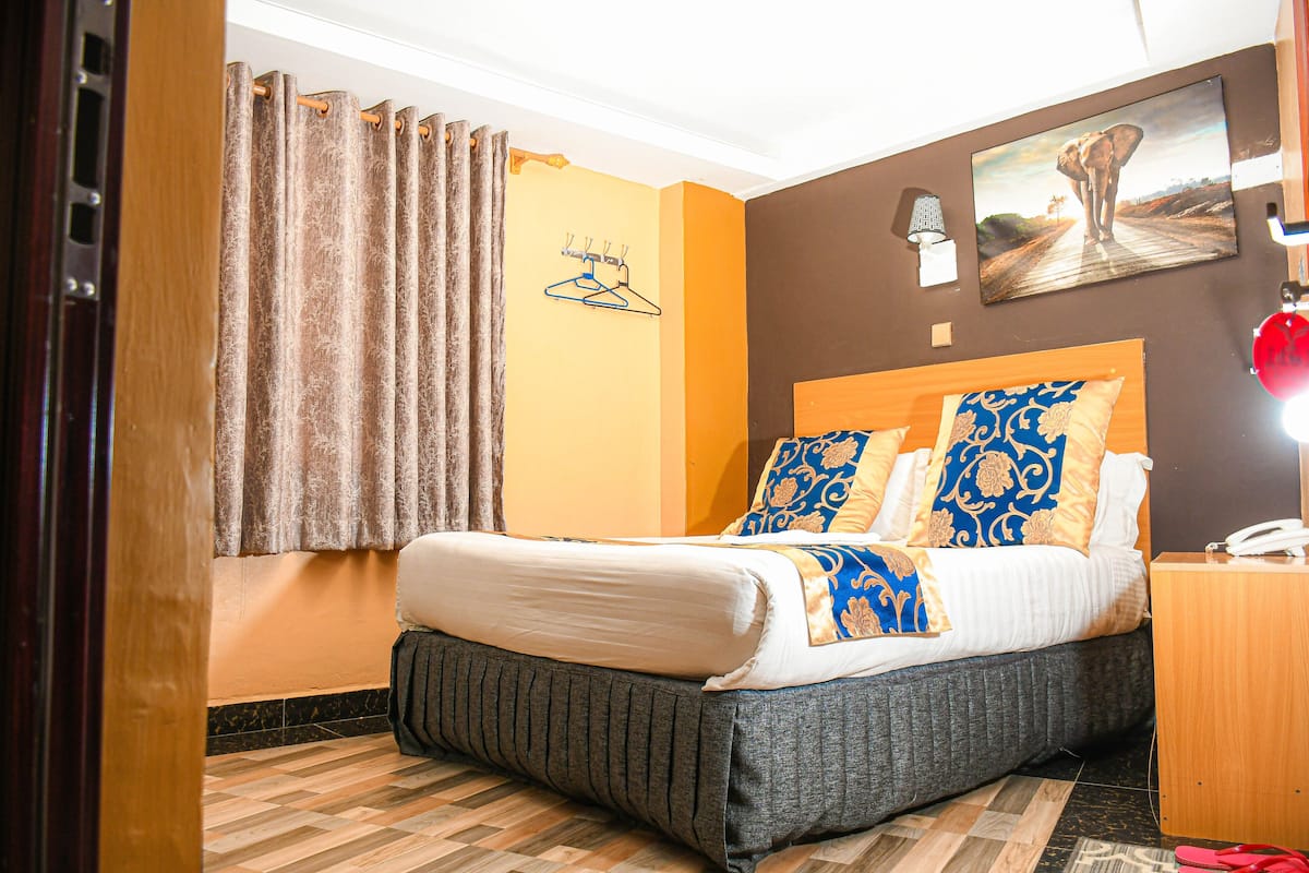 A hotel room with a bed, a wooden nightstand, a lamp, and a painting on the wall.