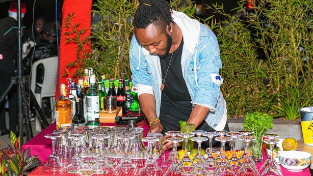 A person arranging glasses and bottles on a table with a red tablecloth, surrounded by various bottles and glasses. - Eaglesvale Resort Naivasha (Naivasha)