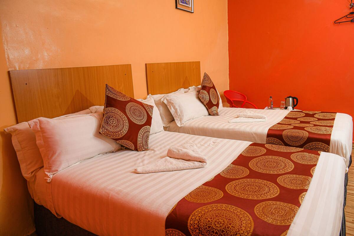 A hotel room with two beds, each with a patterned bedspread, a wooden headboard, and a red chair.