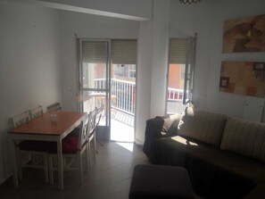 A living room with a sofa, a dining table with chairs, and a balcony with a railing.