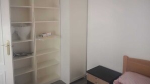 A room with a bed, a small bedside table, and a wardrobe with multiple shelves.