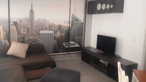 A modern living room with a large window offering a cityscape view, a dark entertainment unit, and a minimalist design.