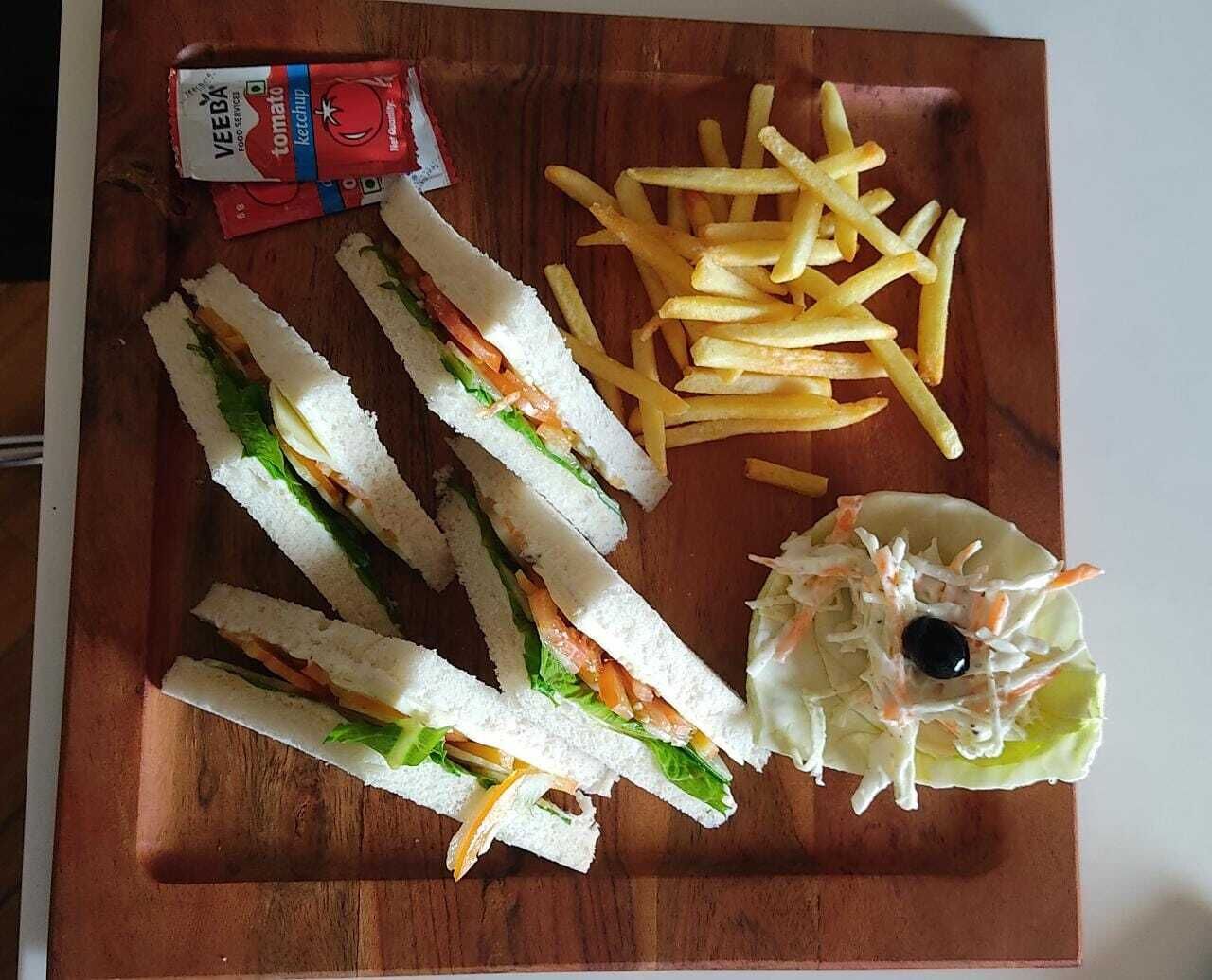 En smörgås som är delad på mitten, pommes frites och en liten sallad med en oliv, serverat på en träbricka.