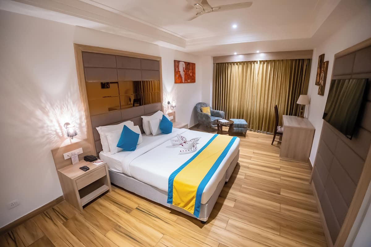 A hotel room with a large bed, a desk, a chair, a TV, and a window with curtains.
