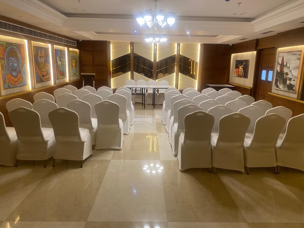 Un salón de conferencias con filas de sillas blancas, un atril y obras de arte en las paredes.