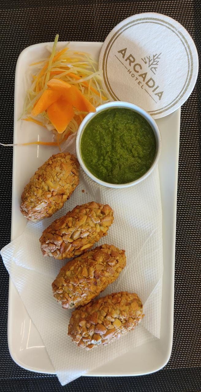 A tray with fried chicken wings, shredded carrots, and a bowl of green sauce, labeled "ARCADIA HOTEL".