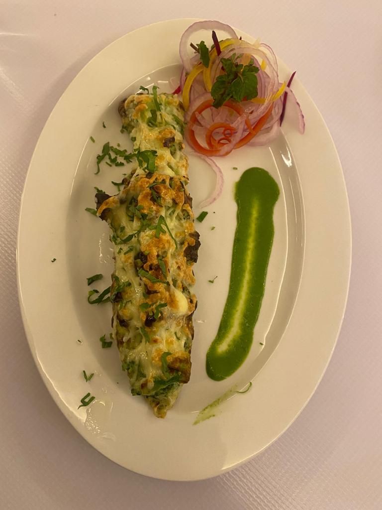 Un plato blanco con un pastel enrollado, posiblemente una pieza de repostería, decorado con hierbas y acompañado de salsa verde, cebollas y rábanos en rodajas finas.