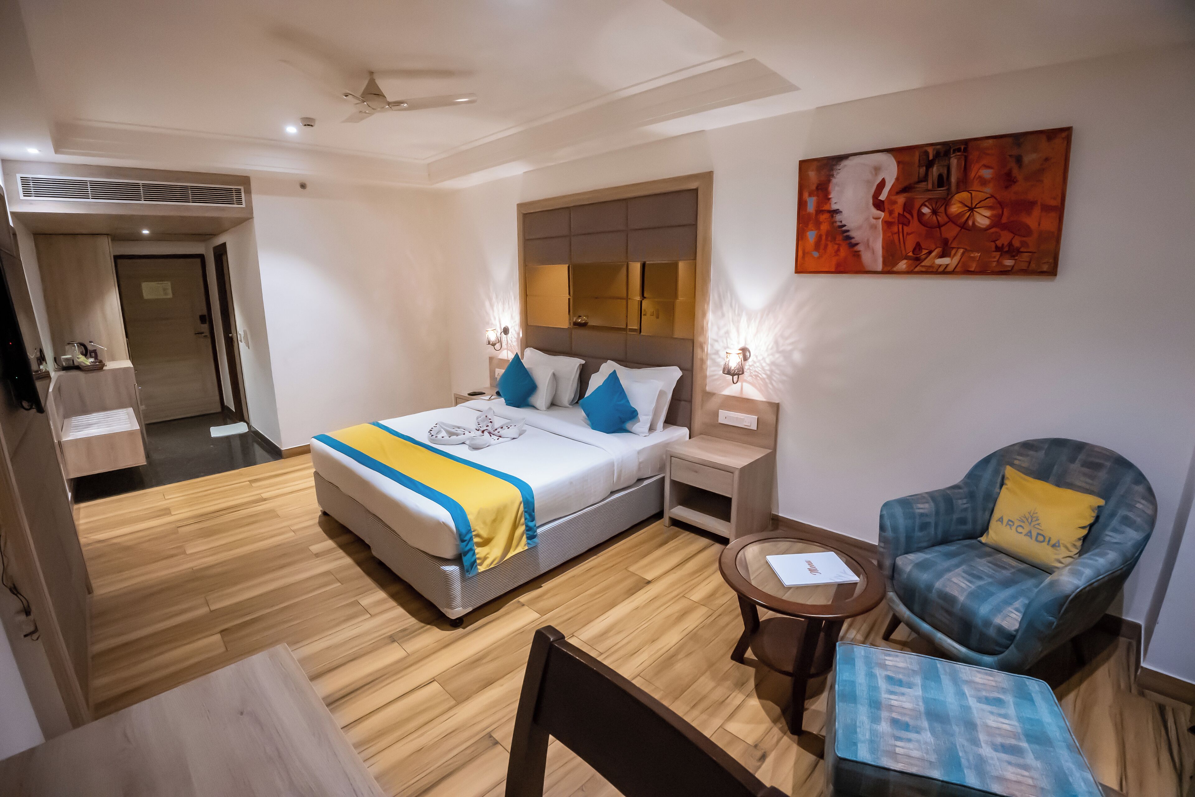 Habitación de hotel con cama, mesitas de noche, una silla, una mesita pequeña y un cuadro en la pared.