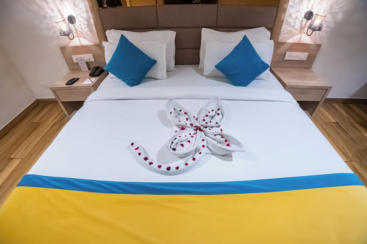 A neatly made bed with a towel arranged in a bow shape, white bedding, and blue pillows.