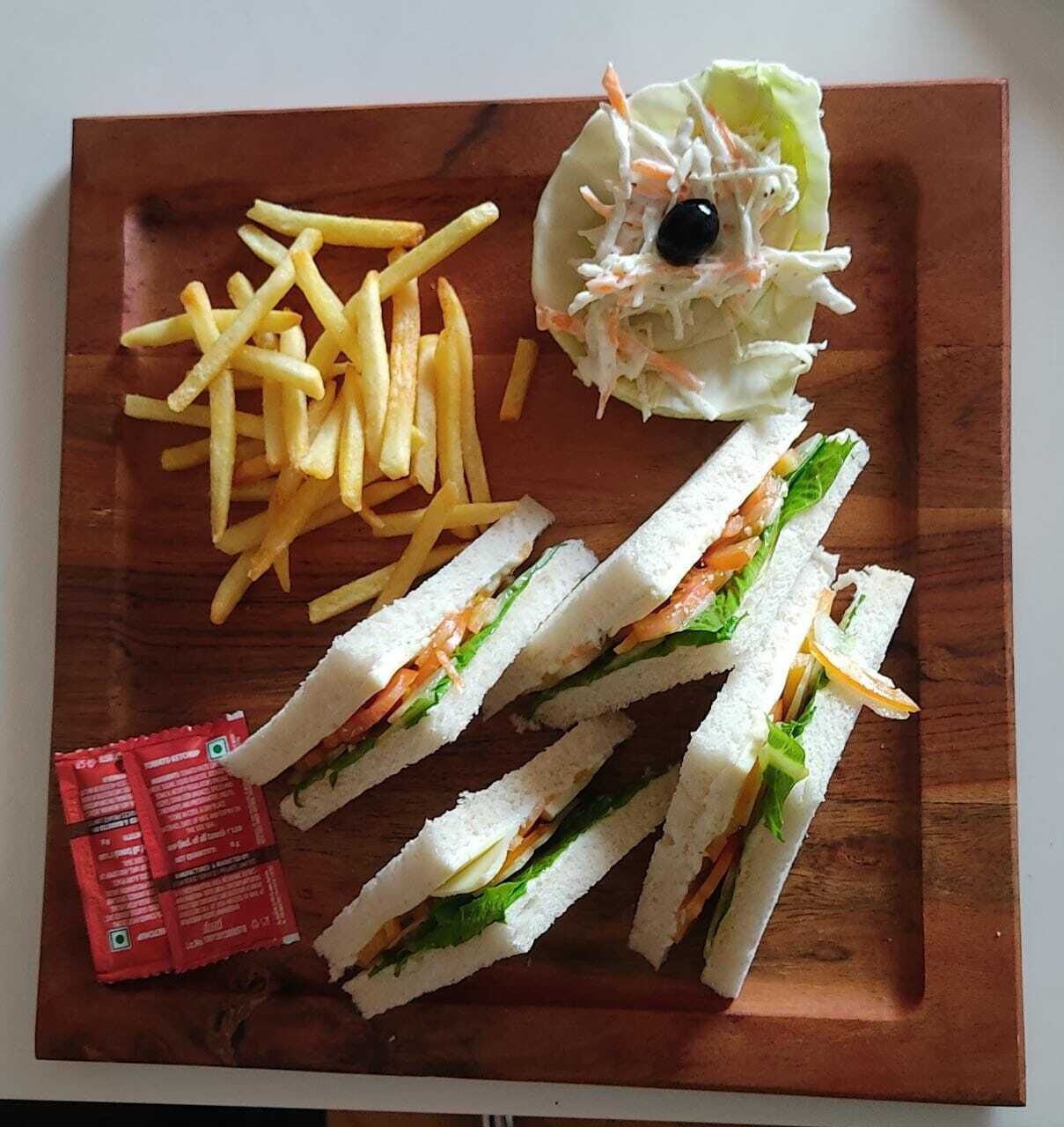 A sandwich with lettuce and cheese, French fries, and a side salad with a black olive on a wooden board.