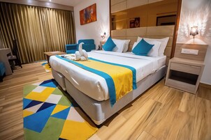 Una habitación de hotel con una cama grande, un escritorio, una silla, un sofá y un televisor instalado en la pared.