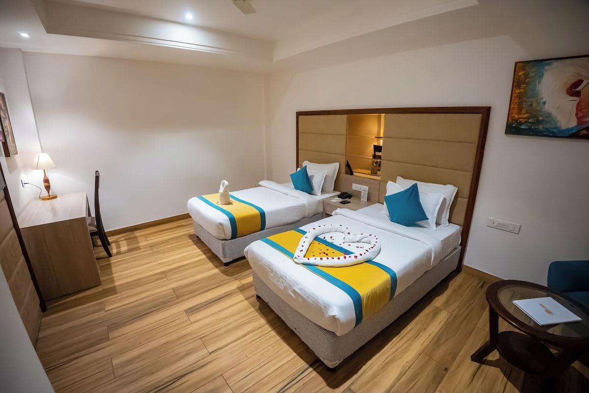 A hotel room with two beds, a small table, a chair, and a lamp.