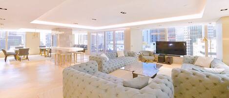 A spacious living area with a large sectional sofa, a flat-screen TV, and a dining area with a high table and chairs.