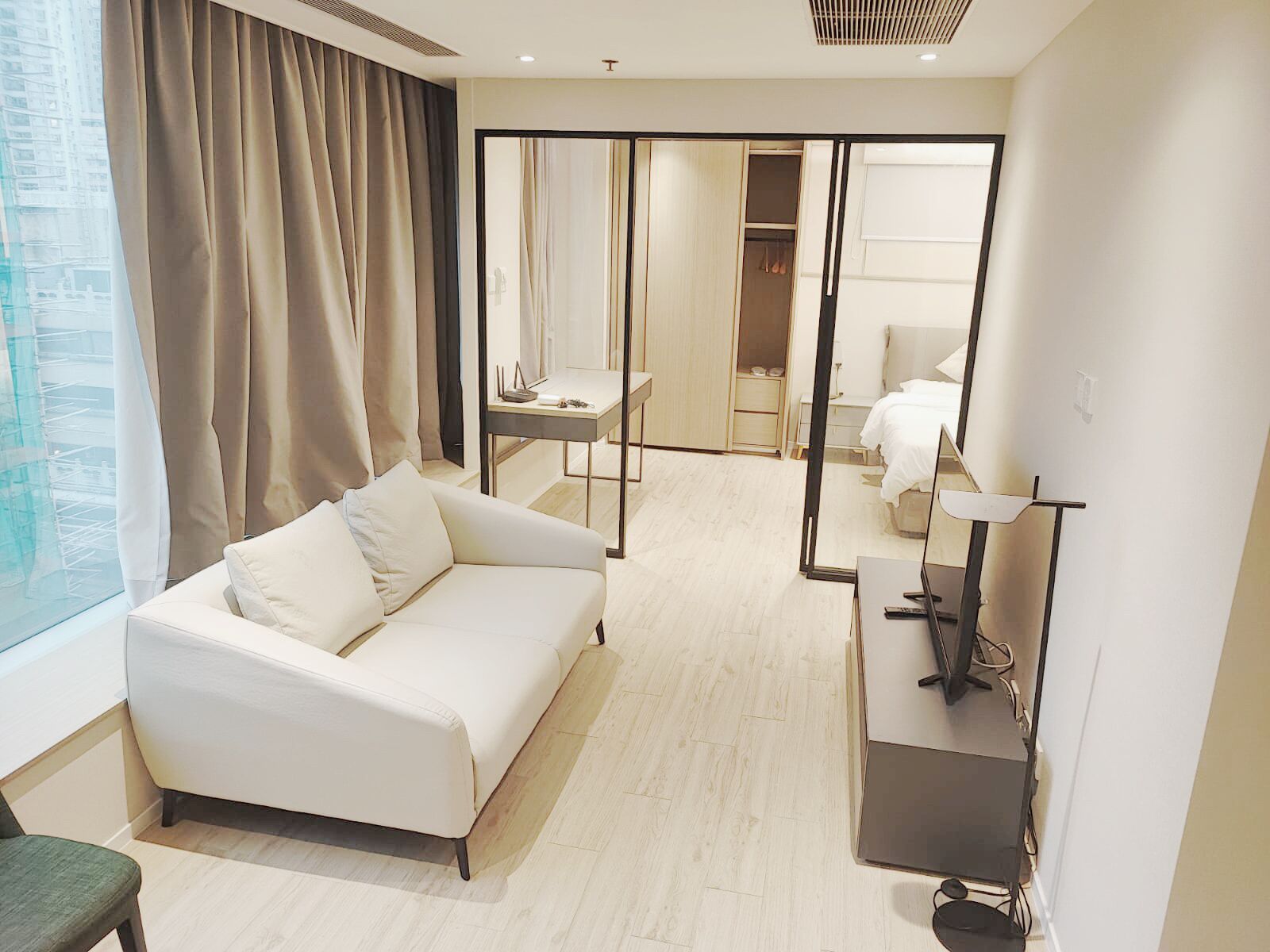 Habitación de hotel moderna con sofá blanco, escritorio con computadora, espejo y armario.