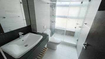 A modern bathroom with a large sink, toilet, and glass-enclosed shower.