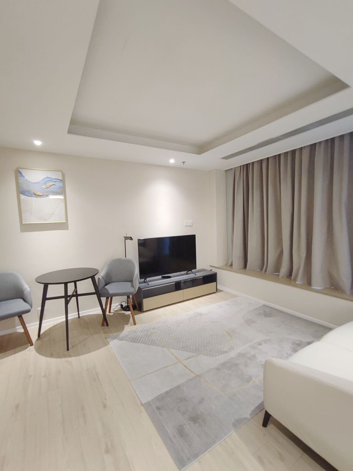 A modern living room with a flat-screen TV, a sofa, a small table, and a painting on the wall.