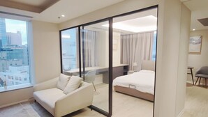 Habitació d'hotel moderna amb un finestral gran, un sofà, un llit i un escriptori.