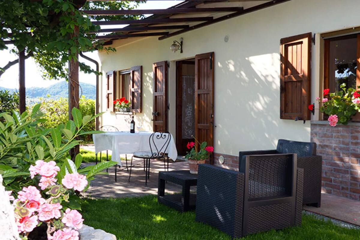 A patio with wicker furniture, a table, and chairs, surrounded by a garden with pink flowers and a view of mountains.