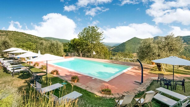 A rectangular pool surrounded by lounge chairs and umbrellas, set against a backdrop of green hills and a clear sky. - Tranquil Farmhouse in Umbria (Monte Santa Maria Tiberina)