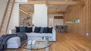 A modern living room with a glass coffee table, grey sofa, wooden beams, and a kitchen in the background. - Homerunner by H2 Life (Kutchan)