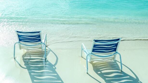 Two empty lounge chairs facing a clear turquoise sea with a sandy beach. - Luxury 3 Bed Palm Beach Strip Condo! (Noord)
