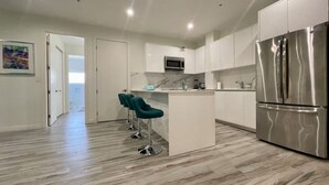 A modern kitchen with white cabinets, a stainless steel refrigerator, and teal bar stools. - Luxury 3 Bed Palm Beach Strip Condo! (Noord)